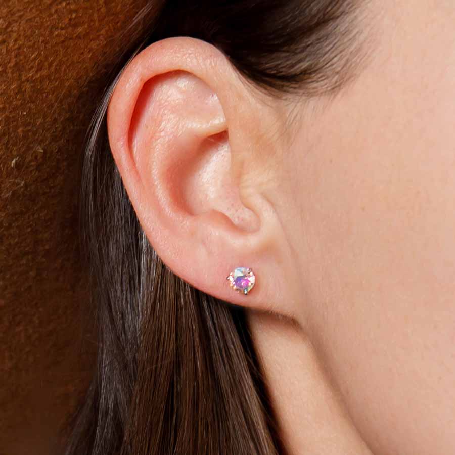 Close-up of an ear wearing a colorful aurora borealis stud earring with a blurred background