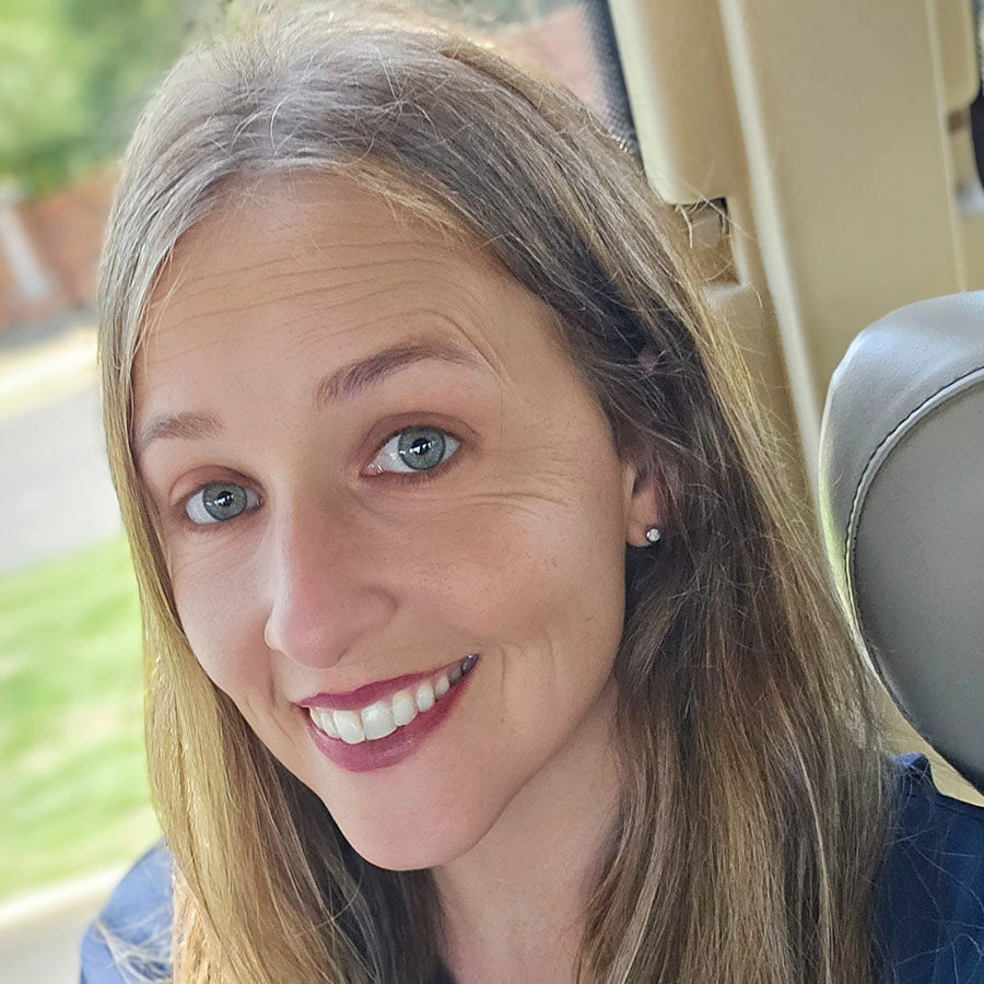 Woman with blonde hair and blue eyes sitting inside a vehicle wearing the White Opal ComfyEarrings.