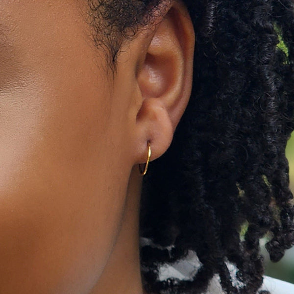 Close-up of an ear wearing a gold hoop earring with dark hair.