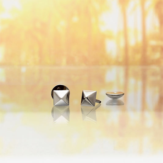 Three silver-toned geometric stud earrings displayed on a reflective surface against a warm, blurred golden background.