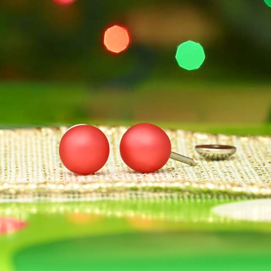 Two red pearl earrings on gold ribbon with blurred colorful lights in the background