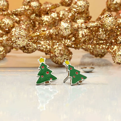 Green Christmas tree earrings with red dots and gold accents on a reflective surface with decorative gold branches in the background.