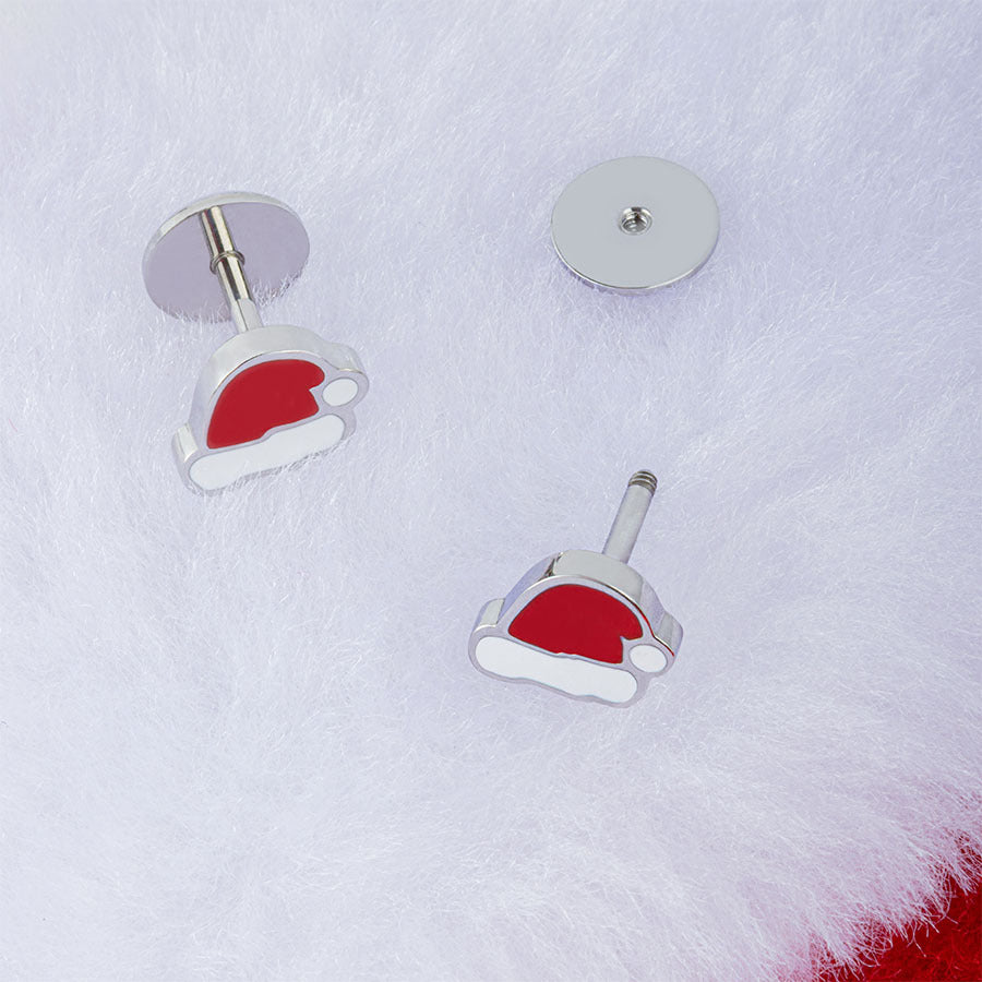 A pair of silver-tone stud earrings shaped like Santa hats with red and white enamel, displayed on a white faux fur background.