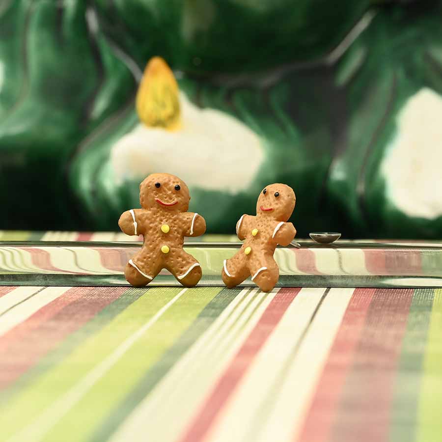 Two gingerbread man earrings on a striped surface with a blurred green and white background.