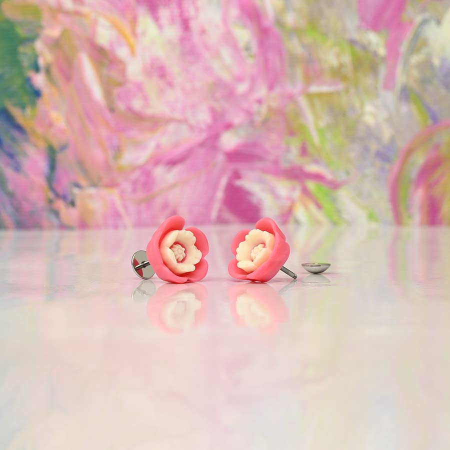 Pink flower-shaped homemade DIY ComfyEarrings on a reflective surface with a colorful, abstract background.