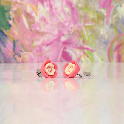 Pink flower-shaped homemade DIY ComfyEarrings on a reflective surface with a colorful, abstract background.