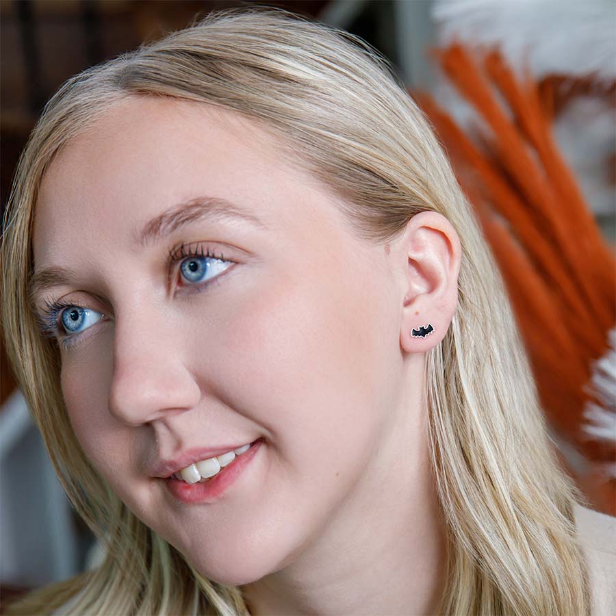 Close-up of a woman wearing a black bat-shaped earring with a blurred background