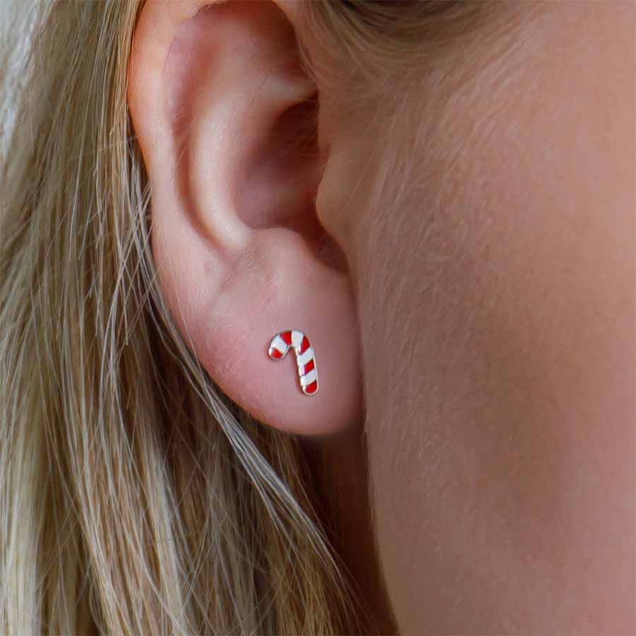 Close-up of an ear wearing a candy cane-shaped earring with blonde hair.