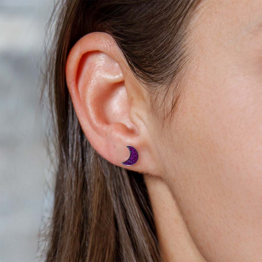 Close-up of an ear wearing a purple moon earring with a blurred background