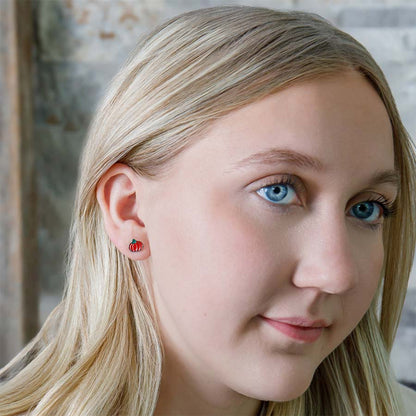 Close-up of a person wearing with small orange pumpkin earrings, against a neutral background.