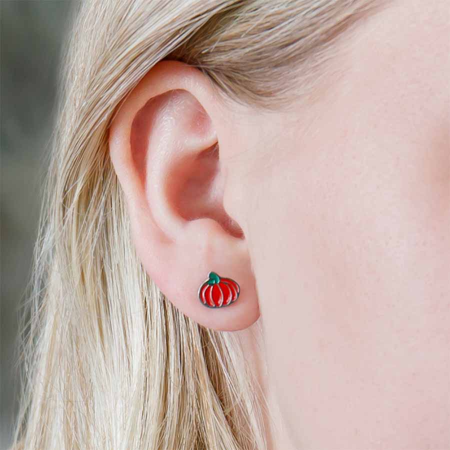Close-up of an ear wearing a pumpkin-shaped earring with a blurred background