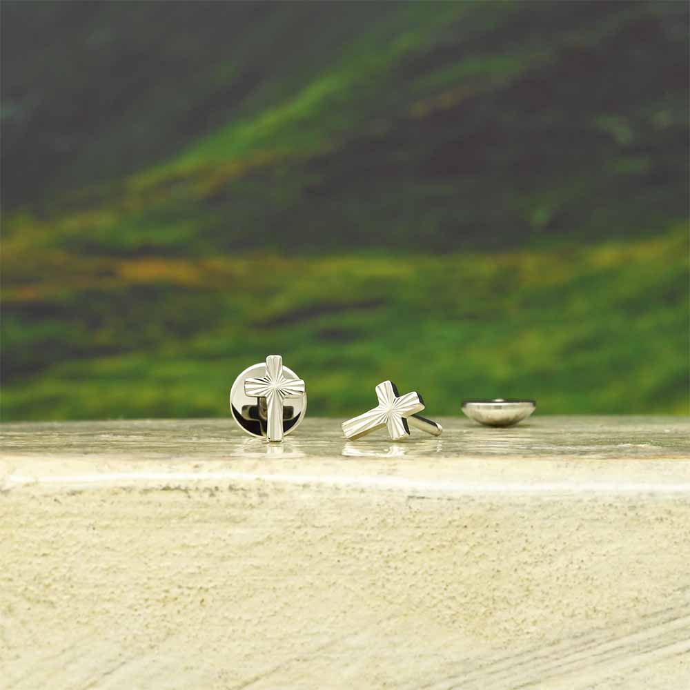 Stainless steel cross-shaped stud earrings on a wooden surface with a blurred natural background