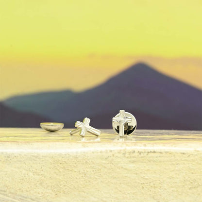 Cross-shaped sleeper earrings on a reflective surface with a mountainous landscape in the background