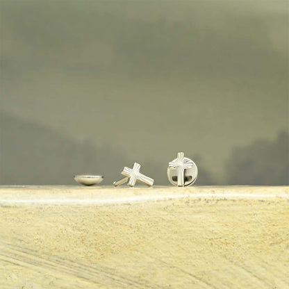 Polished stainless steel Cross Comfy Earrings® on a wooden surface with a blurred background