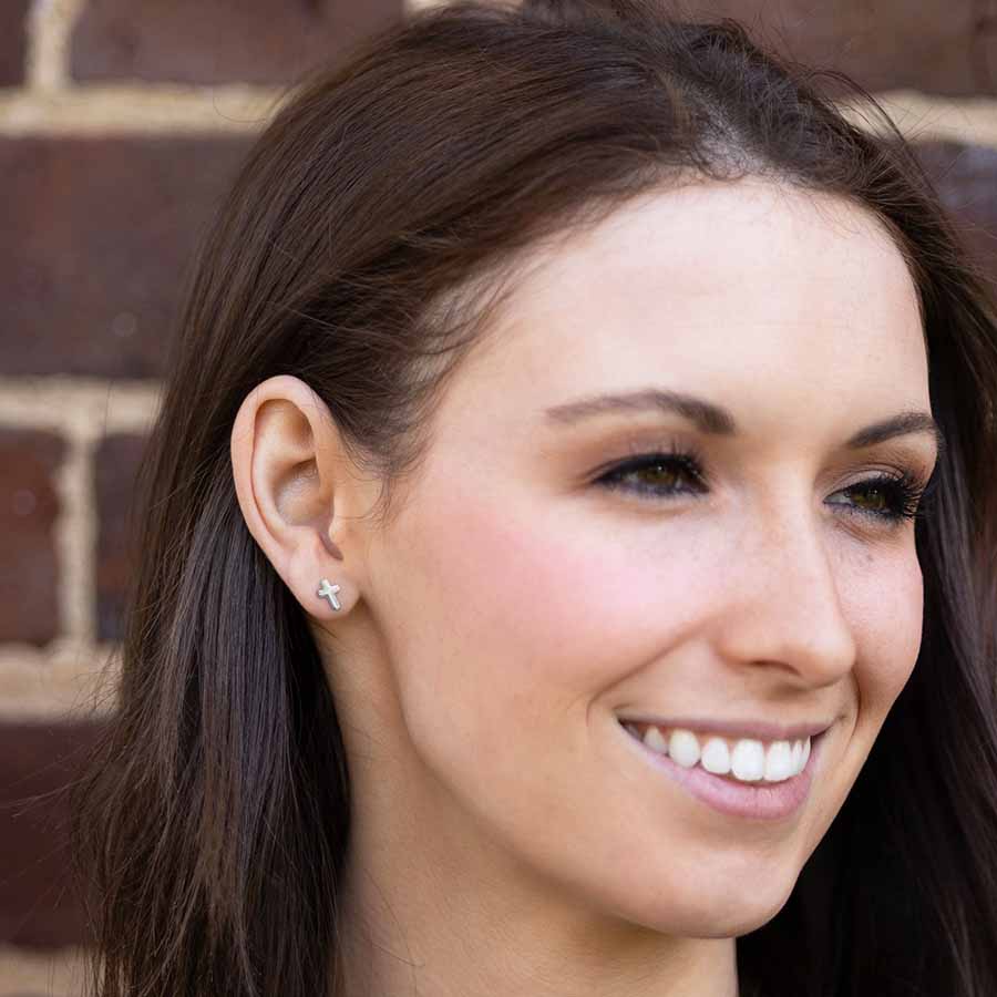 Close-up of a woman wearing a cross shaped stud earring against a brick wall background