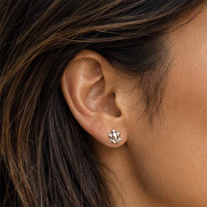 A close-up of a person's ear wearing a small tree frog flat-back earring.