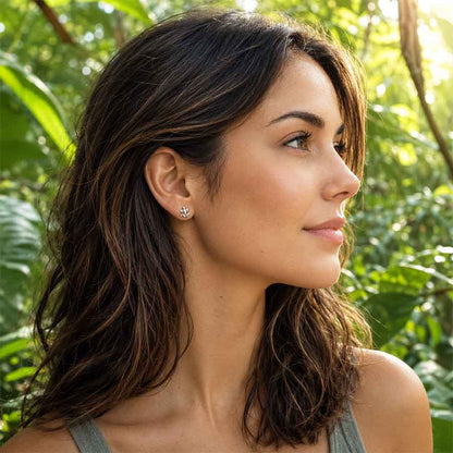 A woman with dark brown hair is shown in profile against a lush green outdoor background, wearing a small frog stud earring.