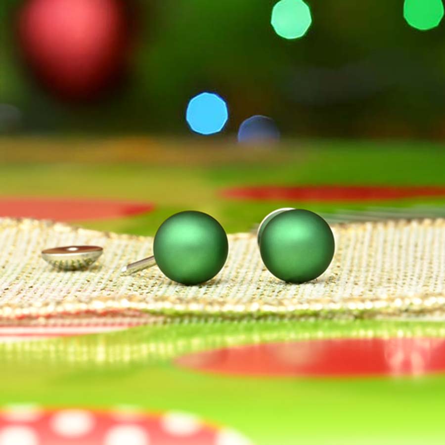 Green round pearl earrings on a textured surface with colorful blurred background