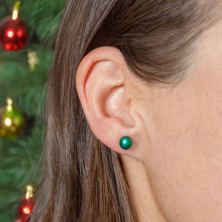Close-up of an ear wearing a green earring with a blurred Christmas tree background