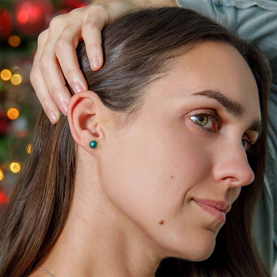 Close-up of a woman wearing green pearl ComfyEarrings with a blurred festive background