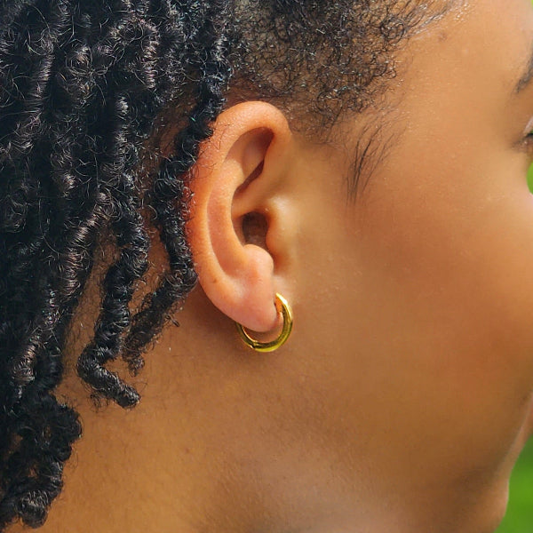 Close-up of an ear with a gold hoop earring, focusing on the jewelry.