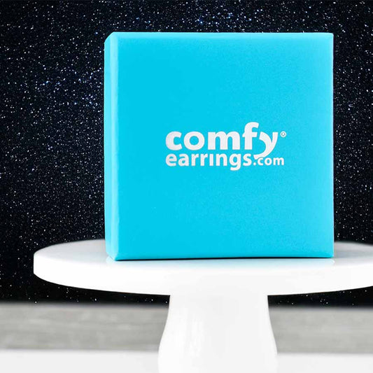 Blue box with 'comfy earrings.com' on a white pedestal against a dark starry sky background