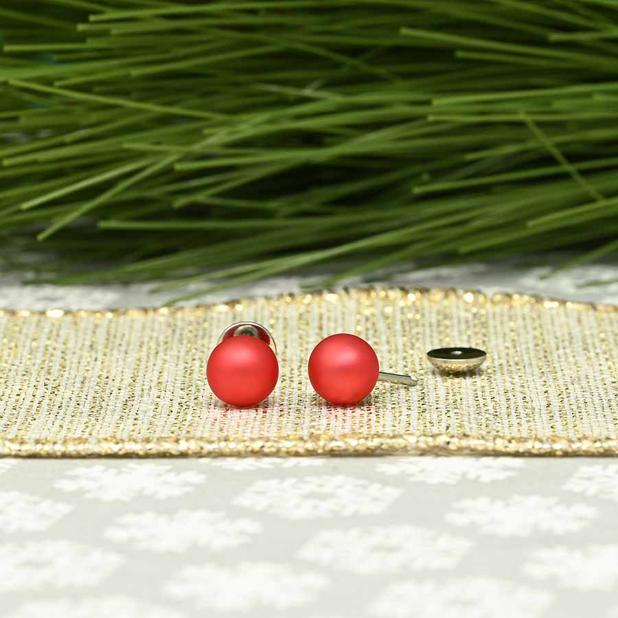 Red pearl Comfy Earrings on a gold surface with greenery in the background