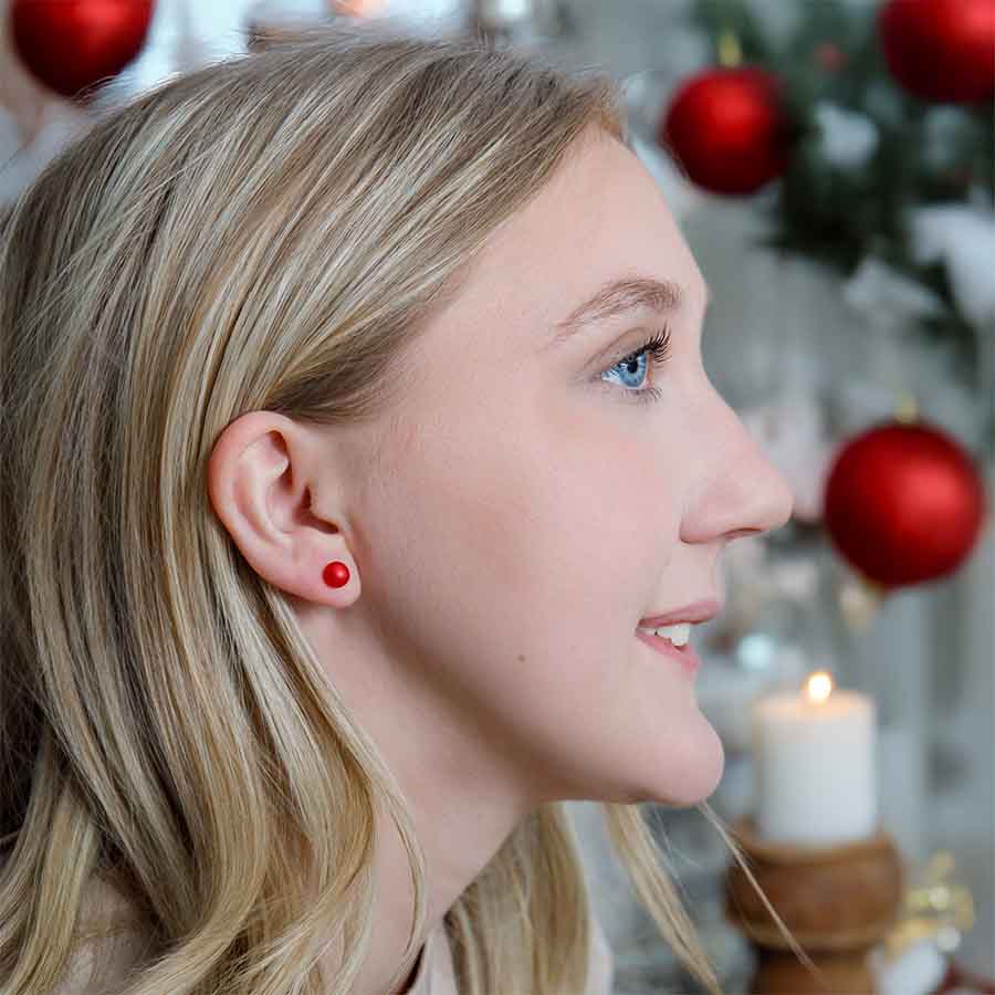 Close-up of a woman wearing read pearl earrings with Christmas decorations in the background