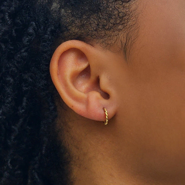 Woman modeling small gold hoop twisted earrings.