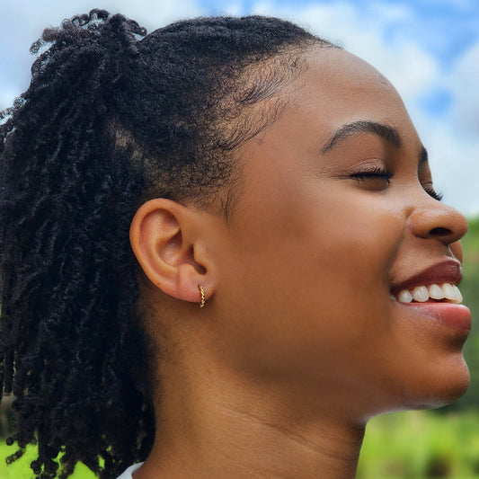 Woman modeling twisted hoop earrings with a blurred natural background