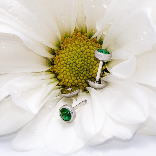 Emerald ComfyEarrings sitting on white flower with water drops.