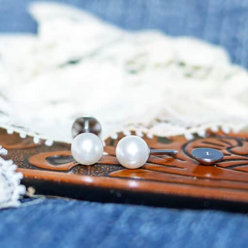 Pearl ComfyEarrings pictured on a brown belt in front of white lace.