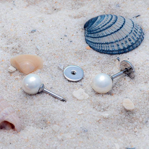 Pearl ComfyEarrings on sand with a blue and tan seashell.