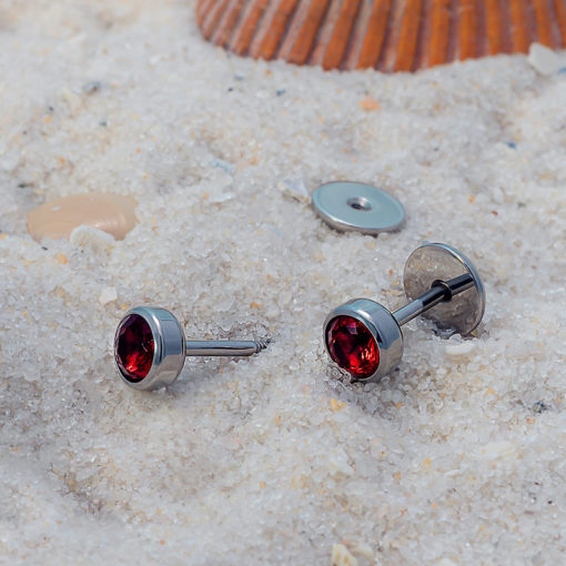 Ruby Red ComfyEarrings on white sand and seashell in background.