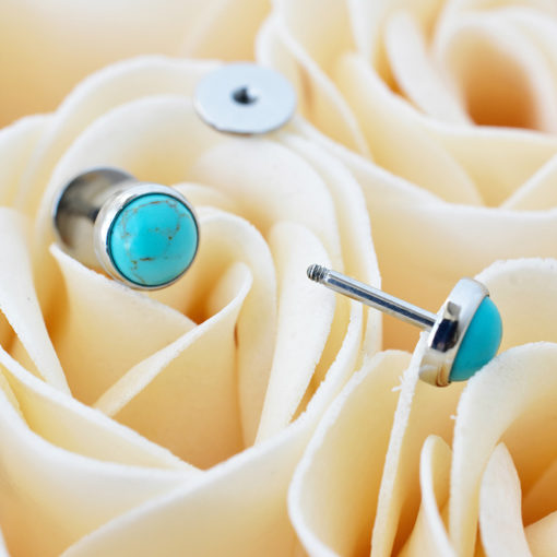 Turquoise ComfyEarrings sitting on cream colored roses up close.