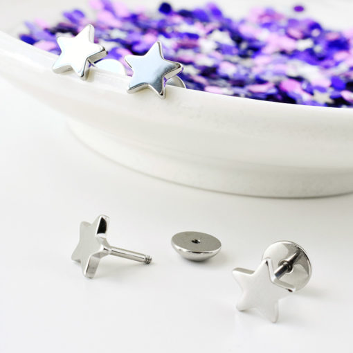 Stainless Star ComfyEarrings on rim of a white dish and unfocused purple decor in background.