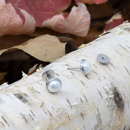 Half Pearl ComfyEarrings sitting on small birch log with fall leaves in background.