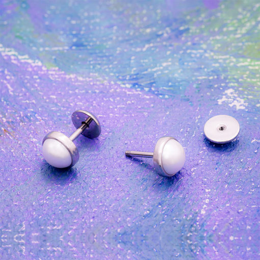Half Pearl ComfyEarrings sitting on purple, blue, and green painting.