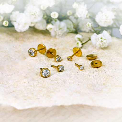 Crystal Clear Gold ComfyEarrings pictured on a stone in front of tiny white flowers.