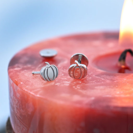Stainless Pumpkin ComfyEarrings on a red and orange candle.