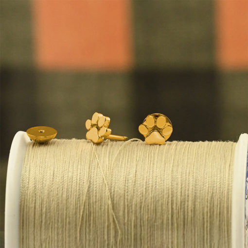 Gold Paw Print ComfyEarrings sitting on a spool of tan sewing thread