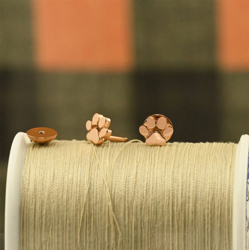 Rose Gold Paw Print ComfyEarrings sitting on a spool of tan sewing thread