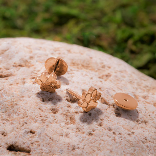 Rose Gold Paw Print ComfyEarrings on a small rock and green moss in the background
