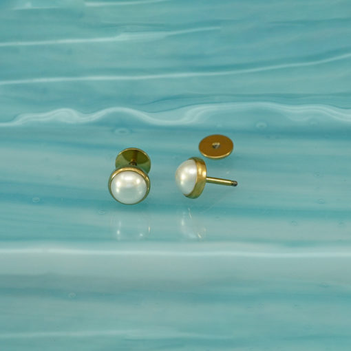 Half Pearl Gold ComfyEarrings sitting on a piece of wavy blue glass.