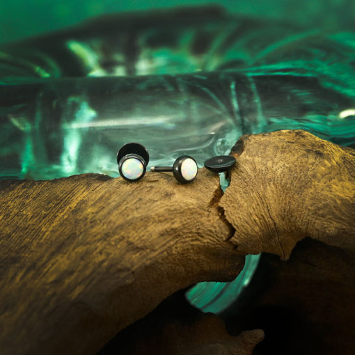 Modern Opal ComfyEarrings sitting on driftwood in front of bluegreen glass.