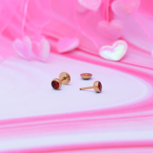 Ruby Red Rose Gold ComfyEarrings sitting on a pink swirl pattern and shiny pink hearts in background.