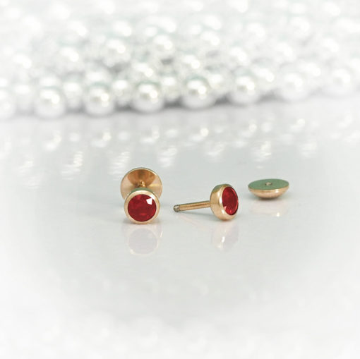 Ruby Red Rose Gold ComfyEarrings on a white dish and silver beads in the background.