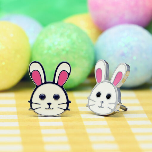 Bunny ComfyEarrings sitting on a yellow and white check tablecloth in front of glitter pastel easter eggs.