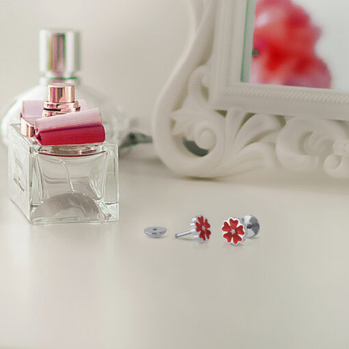 Red Enamel Flower ComfyEarrings sitting in front of a mirror and perfume bottle.