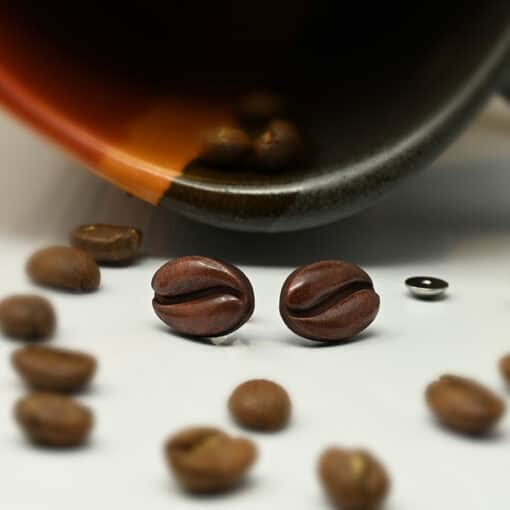 Handmade Coffee Bean ComfyEarrings in front of a coffee mug and scattered coffee beans.